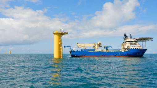 Blue offshore construction vessel with crane equipment near a yellow monopile foundation in open water
