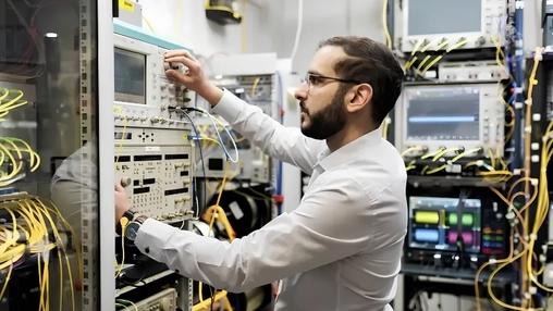 Telecommunications engineer adjusting rack-mounted test gear surrounded by dense yellow fibre optic cables